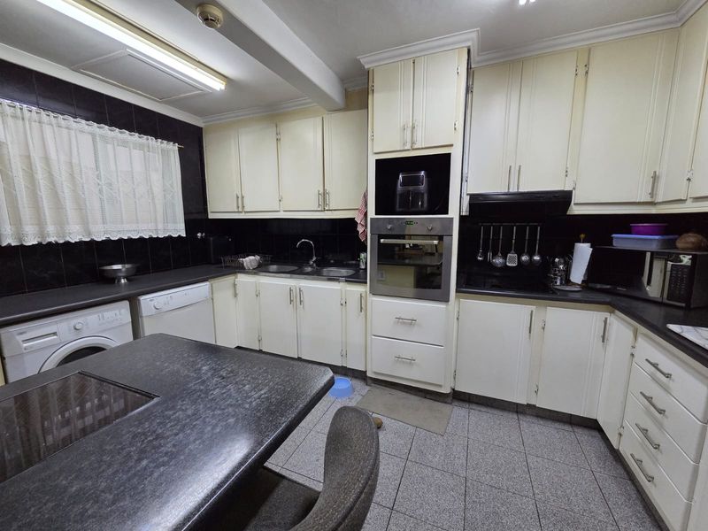 A functional kitchen featuring built-in cabinetry, integrated oven, double sink, and tiled finishes, offering a practical layout with potential for modern updates.