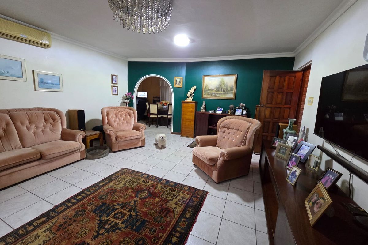 Spacious living room featuring tiled flooring, a decorative archway leading to the dining area, and a prominent crystal chandelier.