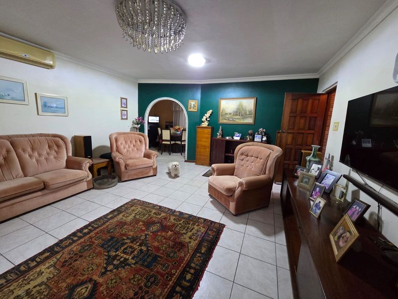 Spacious living room featuring tiled flooring, a decorative archway leading to the dining area, and a prominent crystal chandelier.