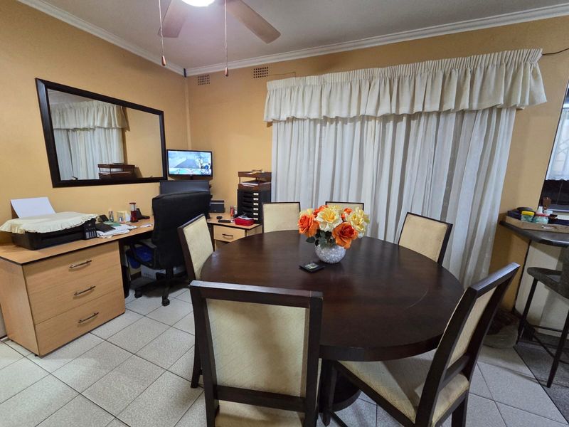 A functional dining area featuring tiled flooring, a ceiling fan, and a built-in desk workspace, offering a versatile layout for dining and home office use.