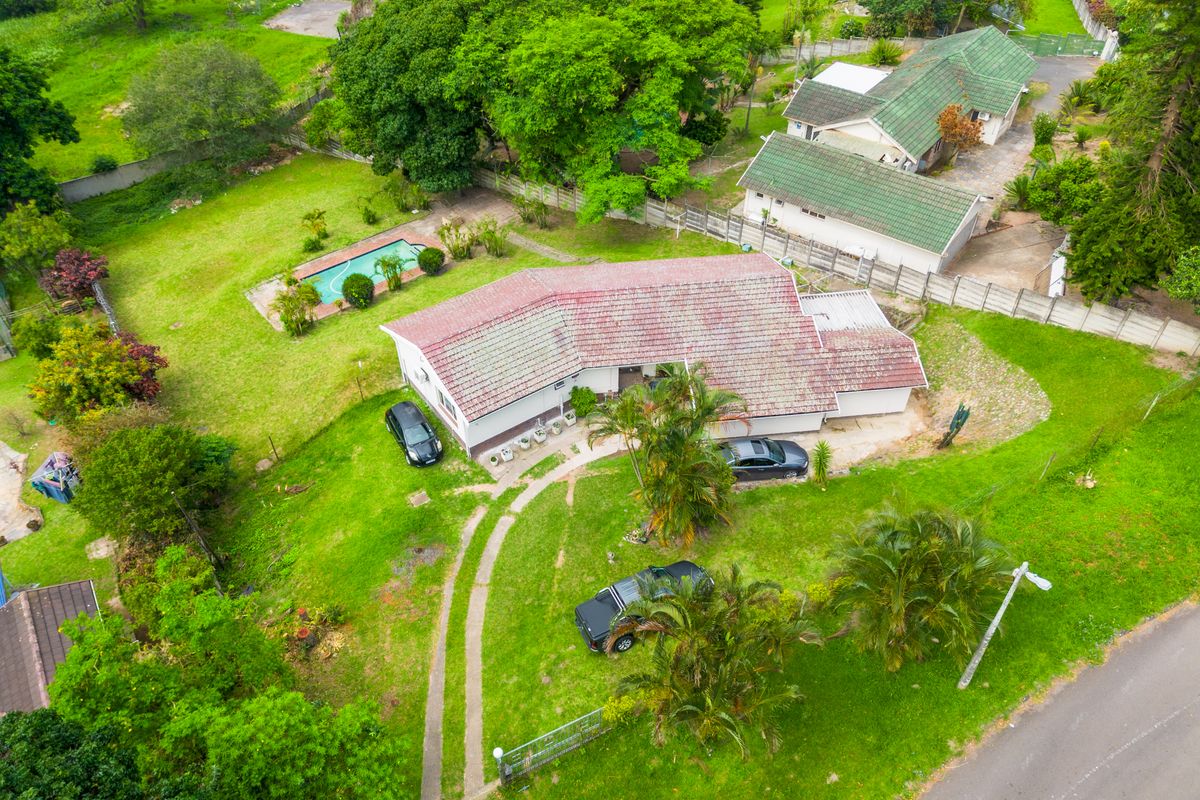 Aerial view of a residential property featuring a large garden, swimming pool, tiled roof dwelling, and a concrete driveway.