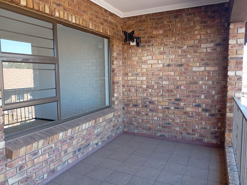 A covered balcony featuring exposed brick walls, tiled flooring, and a metal balustrade, offering a functional outdoor space.