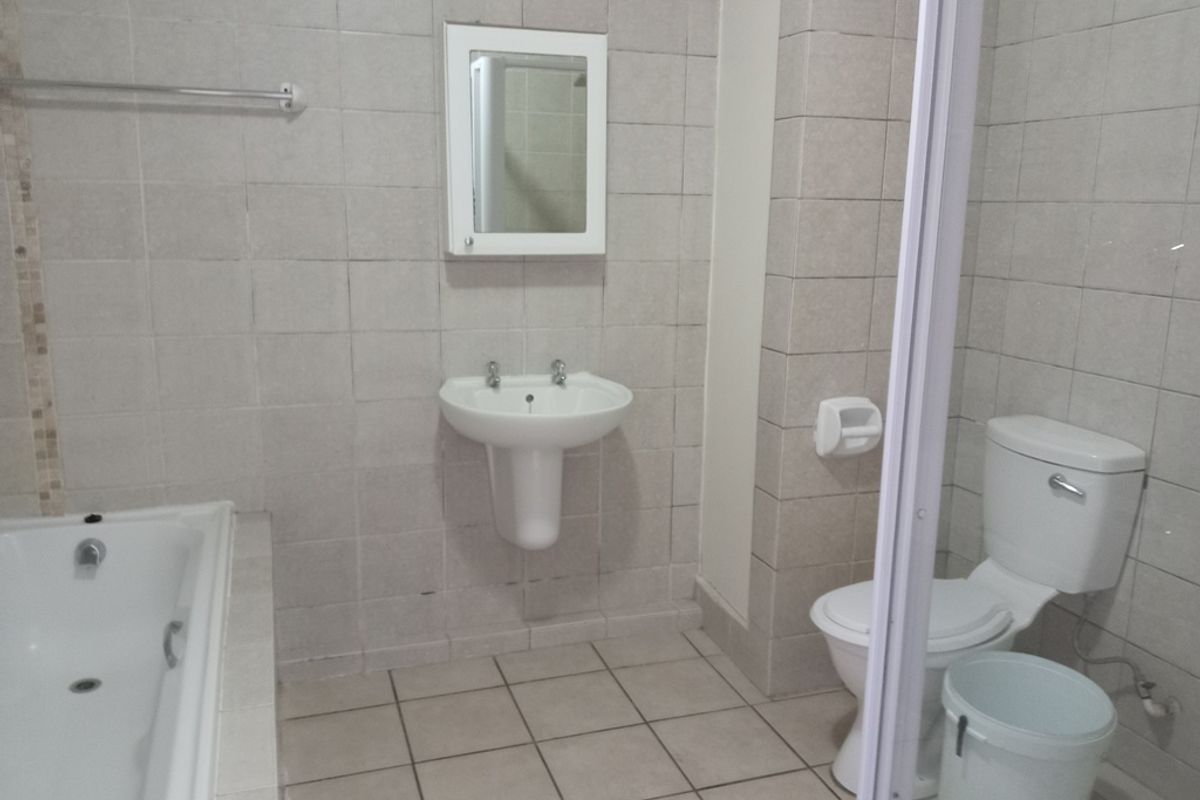 A functional bathroom featuring a built-in bathtub, pedestal basin, and toilet with neutral wall and floor tiling.