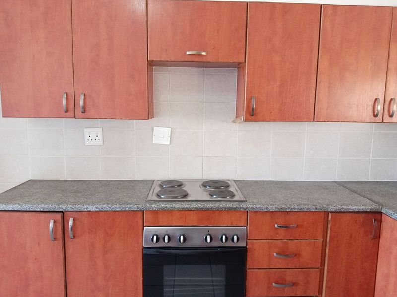 A functional kitchen featuring laminate cabinetry, granite countertops, a built-in oven, and an electric hob with a tiled backsplash.