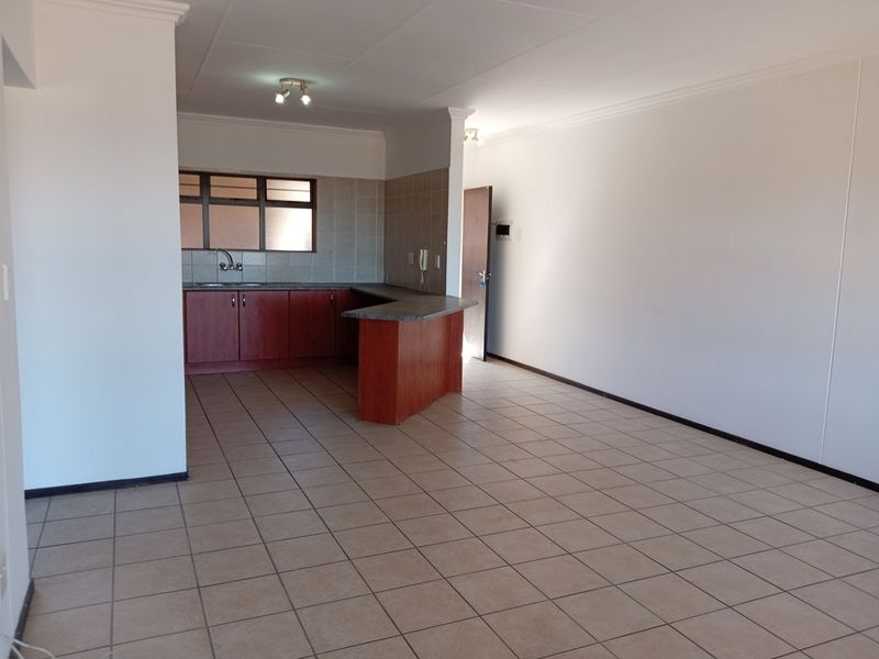 An open-plan living and kitchen area featuring tiled flooring, wooden cabinetry, and a breakfast bar, offering a blank canvas for interior design.