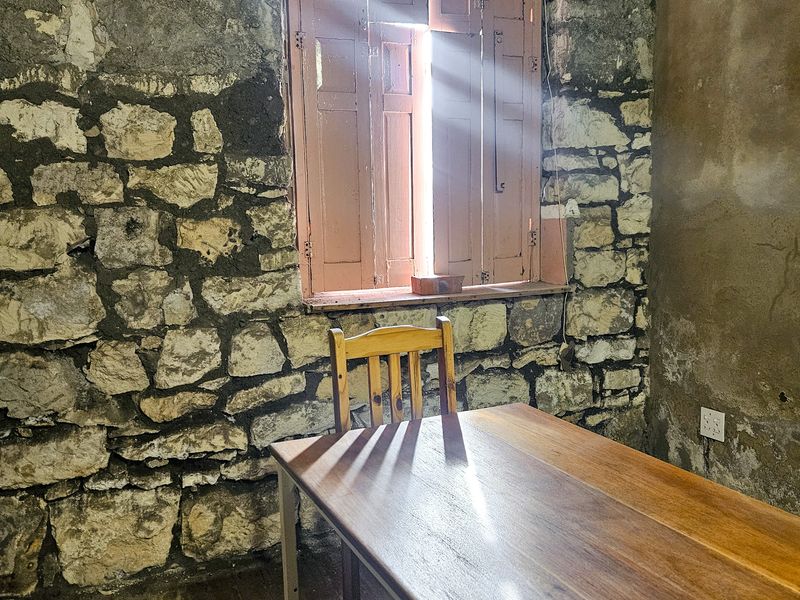 Rustic dining area featuring exposed stone walls, timber flooring, and traditional wooden window shutters, offering a unique historic character.
