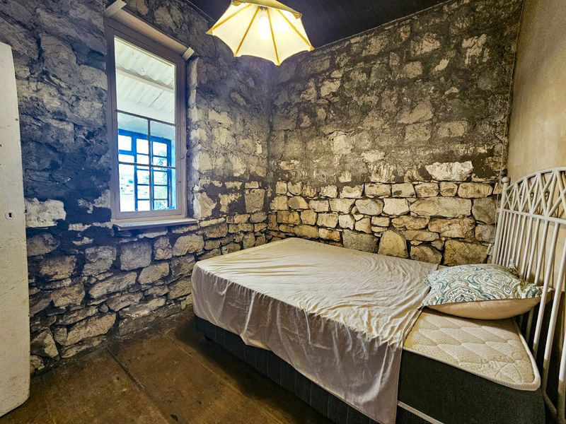 A rustic bedroom featuring exposed stone walls, timber flooring, and a single window, offering a unique character-filled space in need of refurbishment.