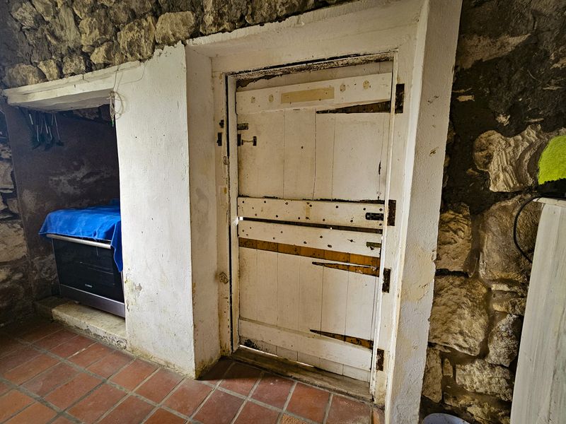Rustic kitchen area featuring exposed stone masonry walls, terracotta floor tiles, and a traditional timber door with a built-in oven.