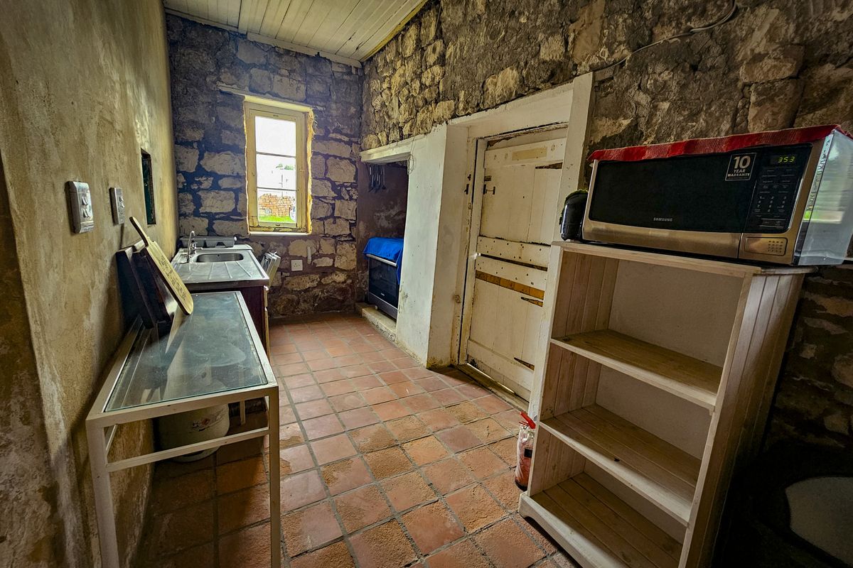 Rustic kitchen featuring exposed stone walls, terracotta flooring, and a timber ceiling, offering a unique character space in need of renovation and modernization.