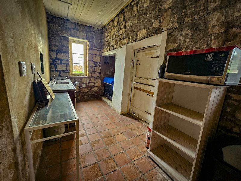 Rustic kitchen featuring exposed stone walls, terracotta flooring, and a timber ceiling, offering a unique character space in need of renovation and modernization.