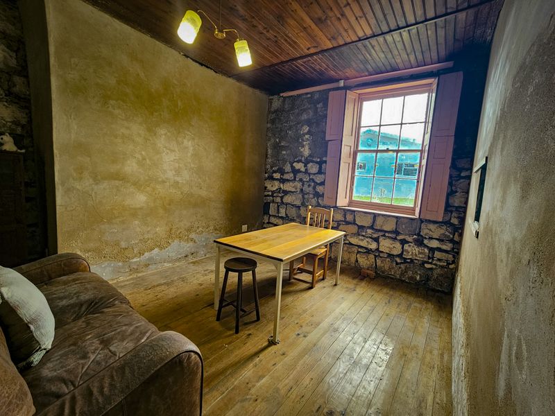 A rustic living area featuring exposed stone walls, timber ceiling, and original timber flooring, requiring significant renovation to restore its character.