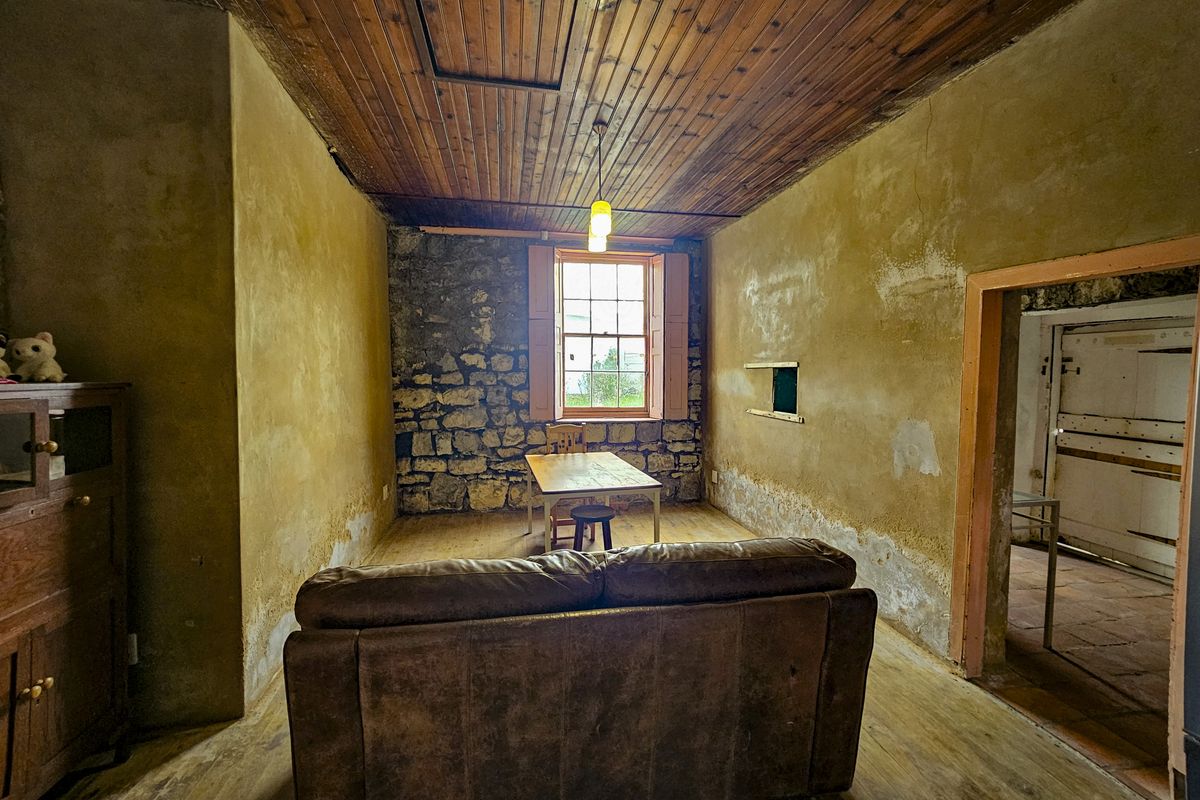 Rustic living room featuring exposed stone wall, timber plank ceiling, and original timber sash window, requiring significant restoration and cosmetic updates.
