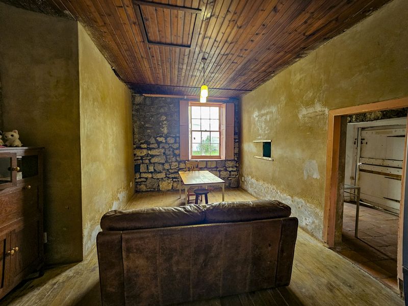 Rustic living room featuring exposed stone wall, timber plank ceiling, and original timber sash window, requiring significant restoration and cosmetic updates.