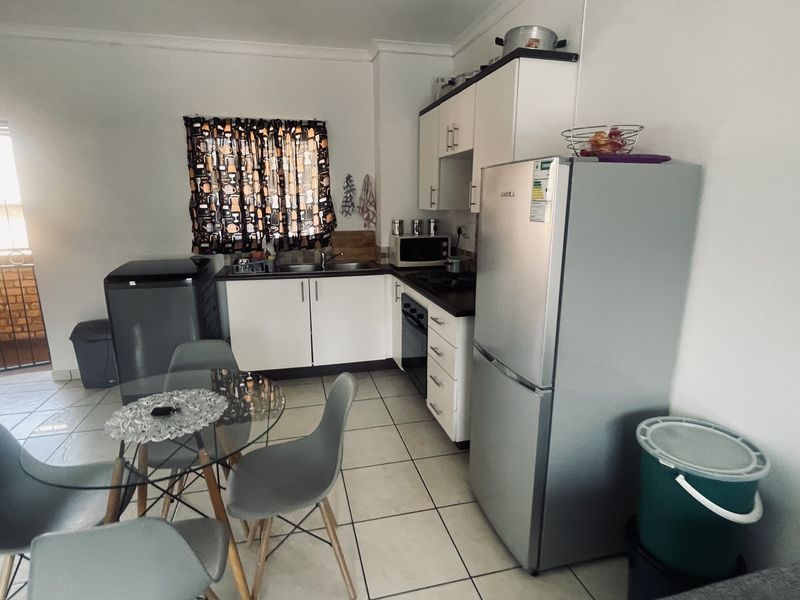 Open-plan kitchen and dining area featuring white cabinetry, laminate countertops, built-in oven, and tiled flooring with direct access to an outdoor balcony.