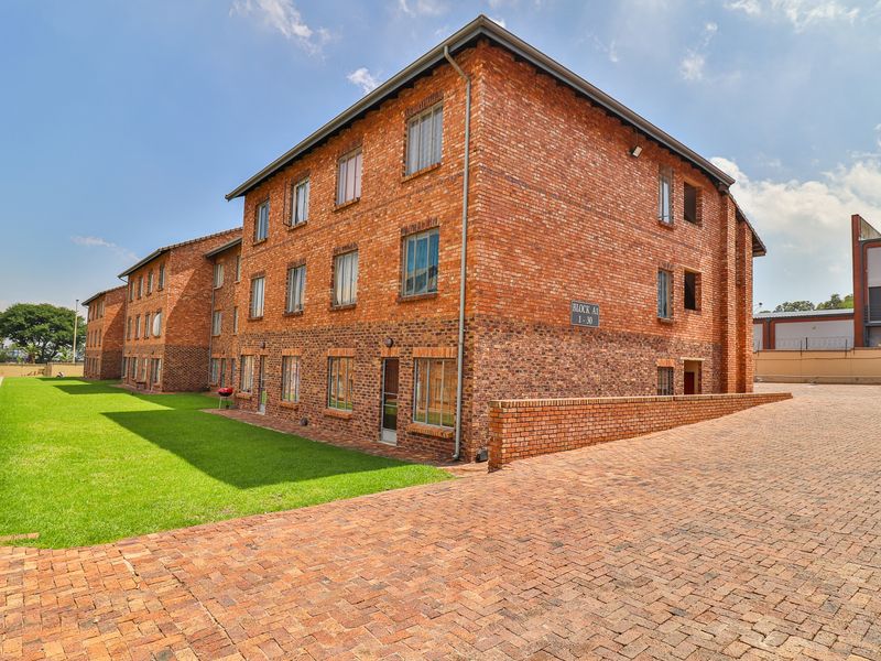 A multi-story apartment building featuring a classic face brick exterior, paved driveway, and well-maintained lawn area.