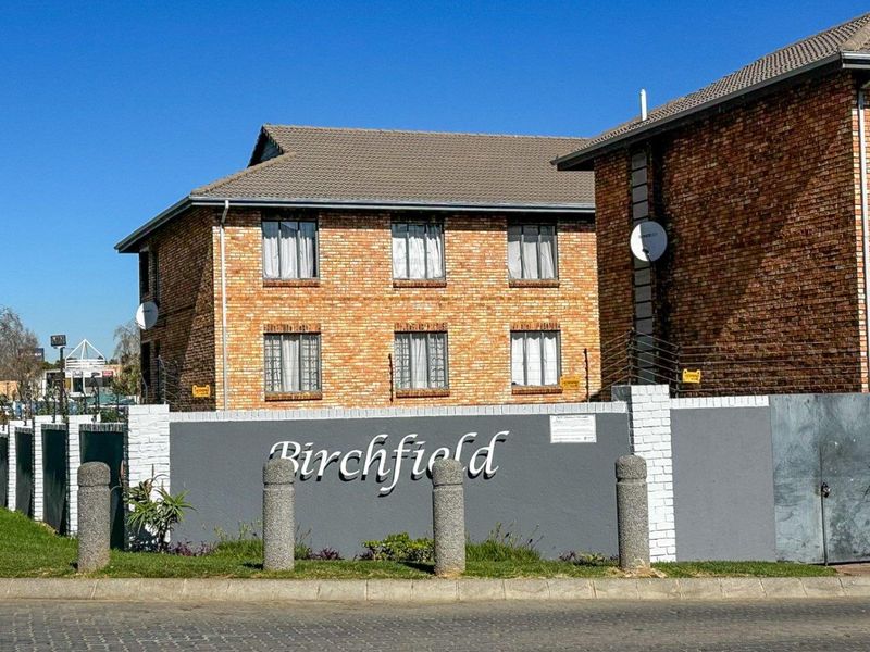 Street view of the Birchfield apartment complex featuring a face brick facade, secure perimeter wall with electric fencing, and gated entrance.