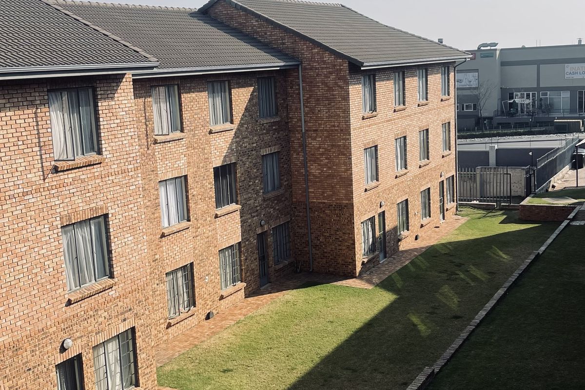 An elevated view of the rear exterior of a multi-story brick apartment building featuring a shared lawn and paved pathways.