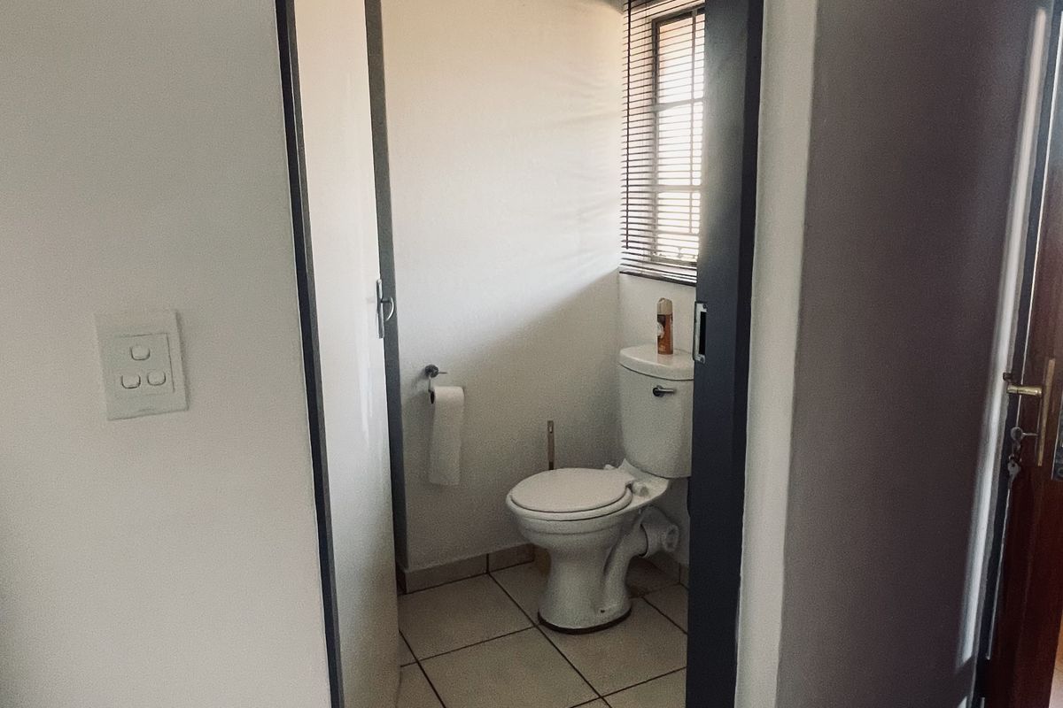 A compact bathroom featuring tiled flooring, a standard toilet, and a window with fitted blinds, providing functional utility space.