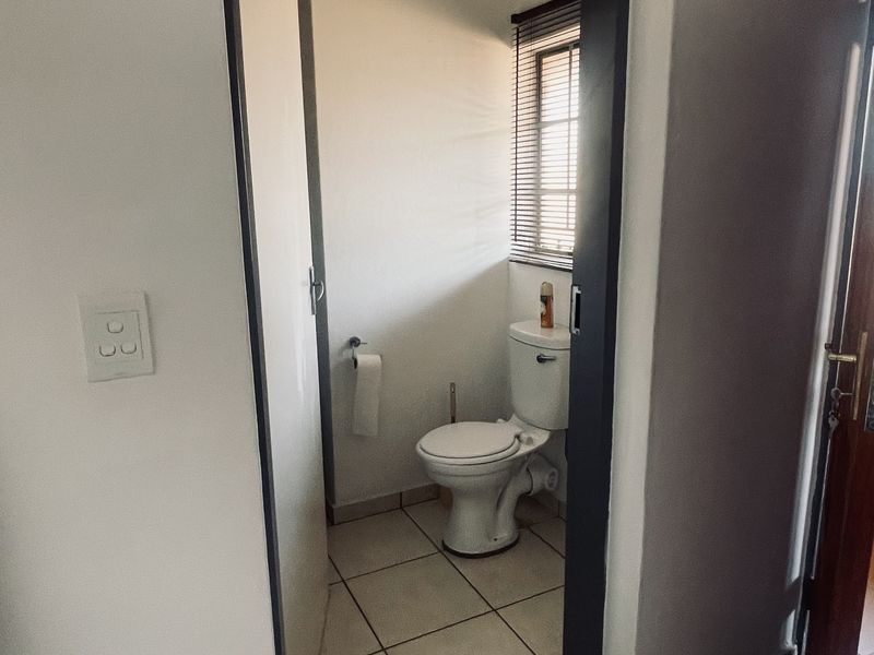 A compact bathroom featuring tiled flooring, a standard toilet, and a window with fitted blinds, providing functional utility space.