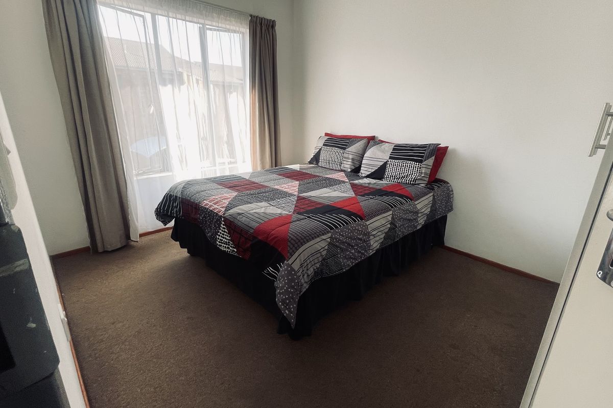 A standard bedroom featuring carpeted flooring and a large window with curtain tracks, providing natural light to the space.