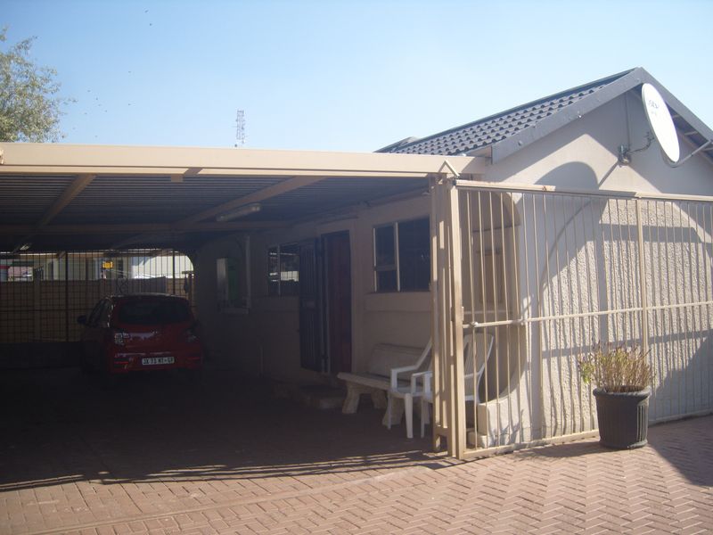 Front exterior view of the property featuring a covered carport, paved driveway, and secure gated entrance.