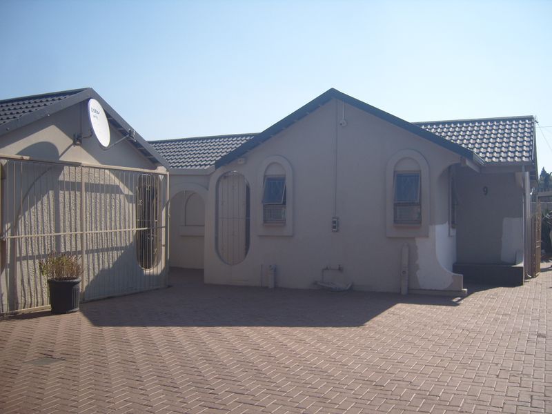Front view of a residential house featuring a paved driveway, tiled roof, and security features, with some exterior wall areas requiring finishing.