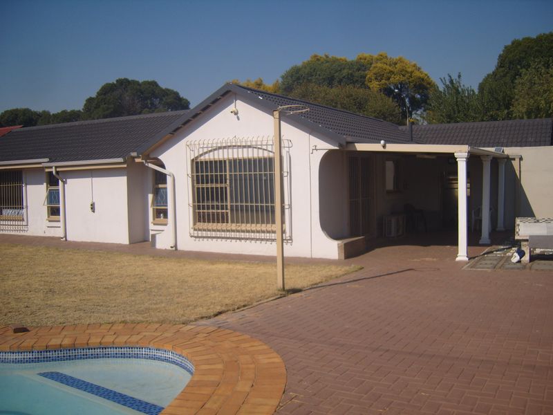 Rear view of the house featuring a tiled roof, covered patio area, and a swimming pool with brick paving.