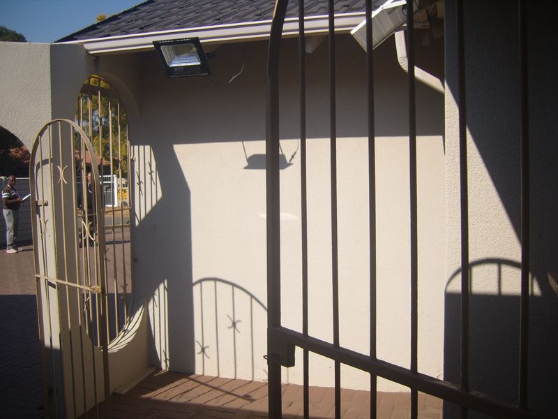 A view of the property entrance featuring a security gate, paved driveway, and exterior floodlight.