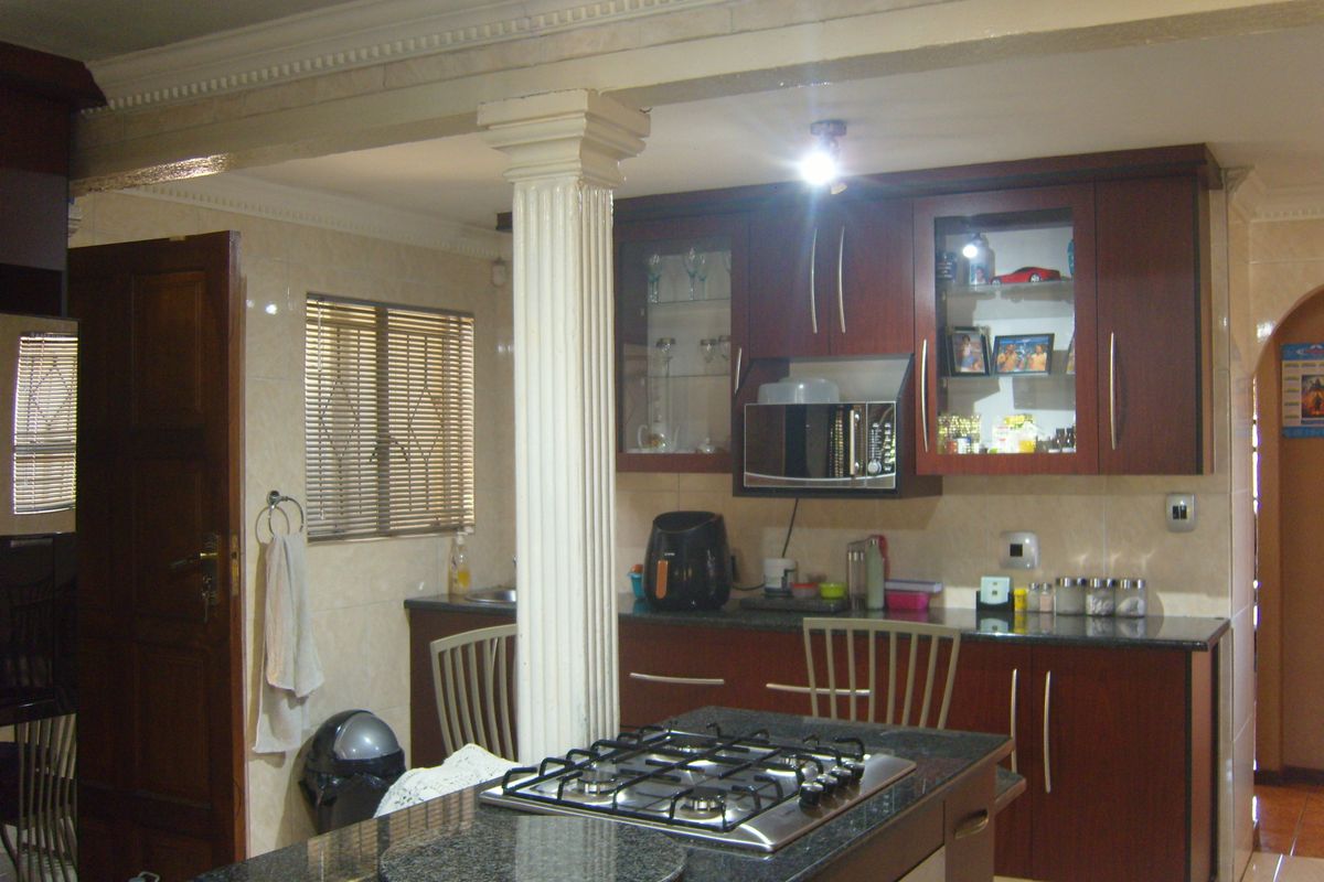 A functional kitchen featuring dark wood cabinetry, granite countertops, a central island with a gas hob, and a decorative structural column.