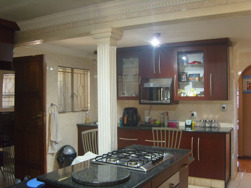 A functional kitchen featuring dark wood cabinetry, granite countertops, a central island with a gas hob, and a decorative structural column.