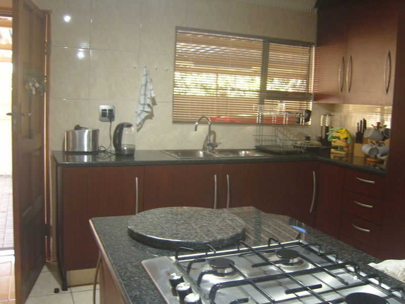 A functional kitchen featuring dark wood cabinetry, granite countertops, a central island with a gas hob, and a double sink with tiled backsplash.