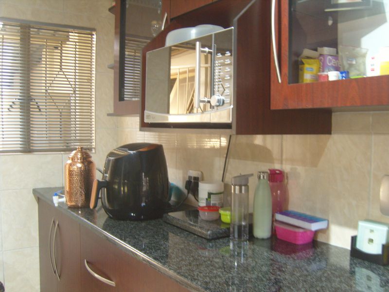 A functional kitchen area featuring dark wood cabinetry, granite countertops, and a built-in microwave with tiled wall finishes.