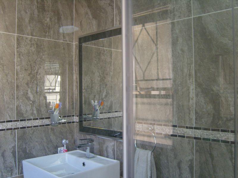 A modern bathroom featuring floor-to-ceiling marble-look wall tiles, a sleek wall-mounted basin with chrome fixtures, and a large framed mirror.