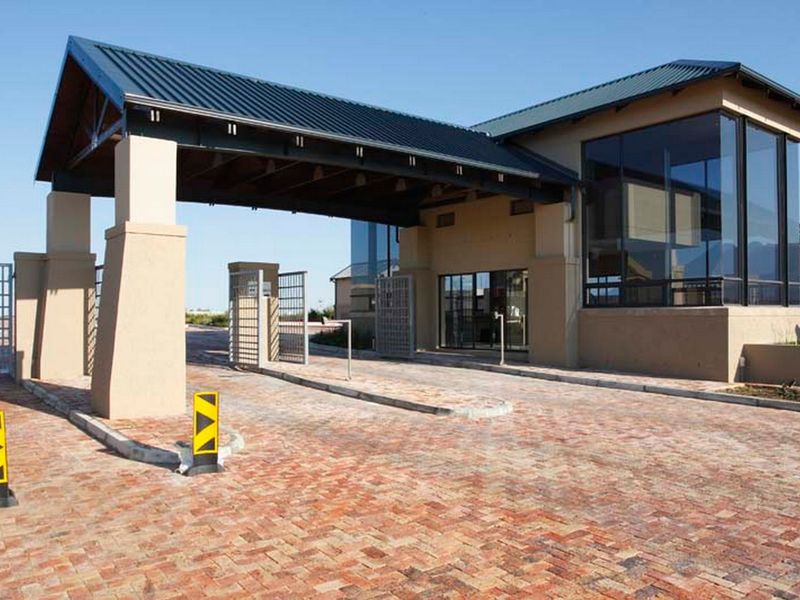 A modern residential estate entrance featuring a brick paved driveway, a covered porte-cochere, and large glass windows.