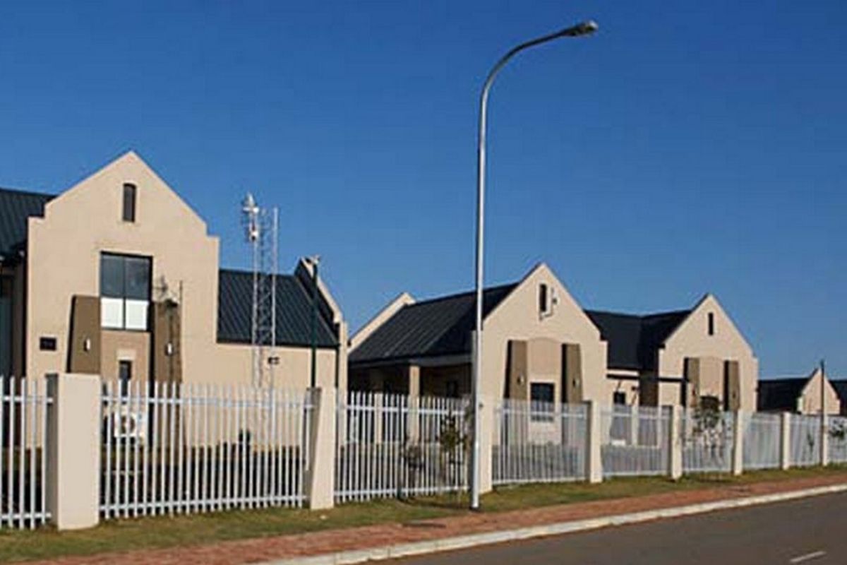 A street-level view of a residential complex featuring modern architectural design with metal roofing, stucco facades, and secure steel picket fencing.