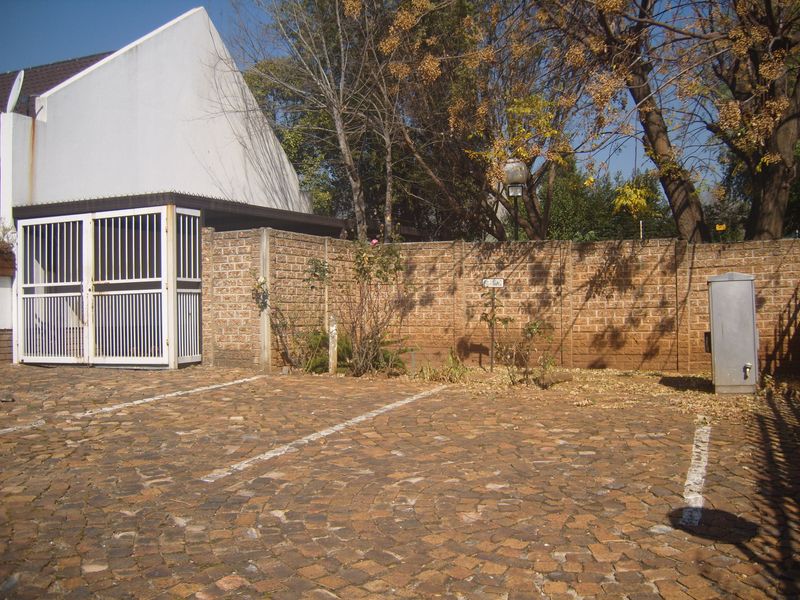 Exterior view of a townhouse driveway featuring cobblestone paving, a secure gated entrance, and a brick boundary wall.