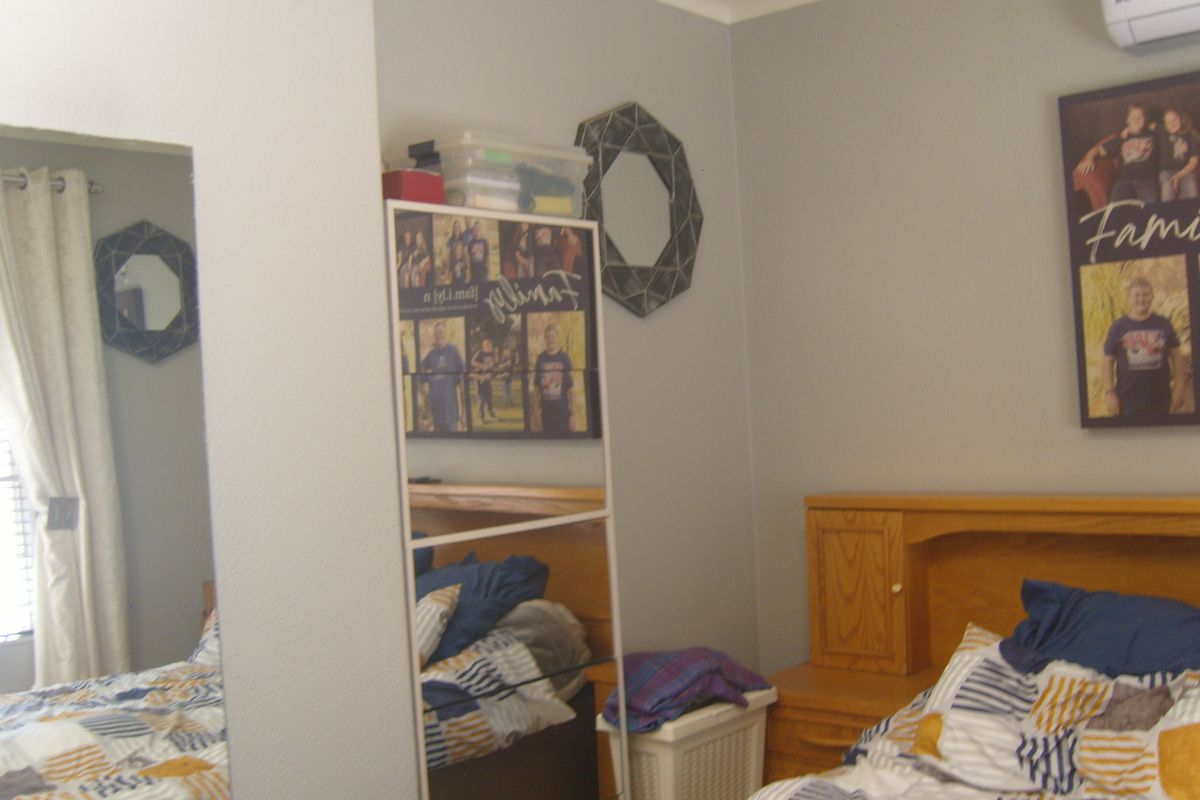 A bedroom featuring a built-in headboard and wall-mounted air conditioning unit, finished with neutral grey walls.