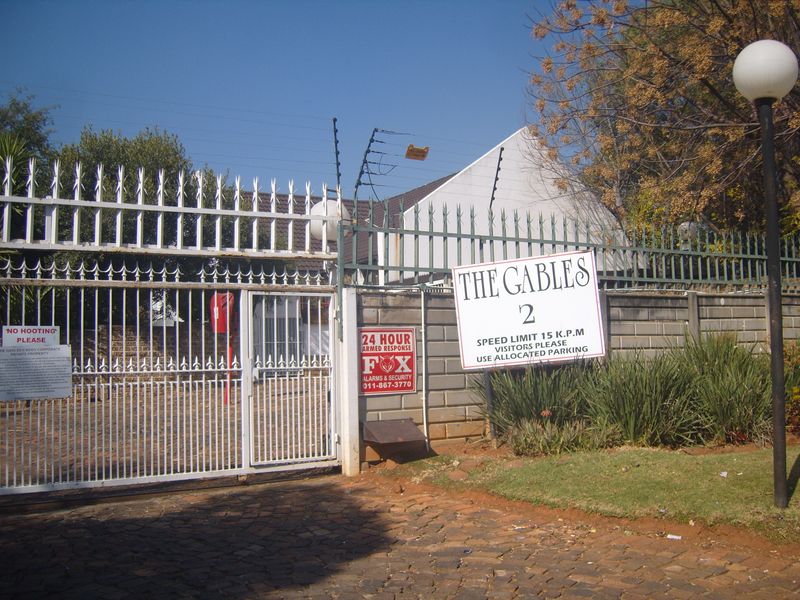 Front entrance view of The Gables complex featuring a secure gated access point with electric fencing and brick boundary walling.