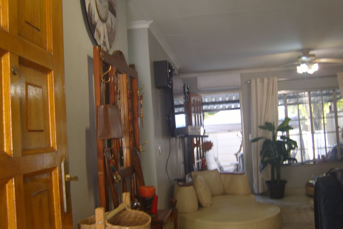 A living room area featuring a ceiling fan, wall-mounted air conditioning unit, and timber door access.
