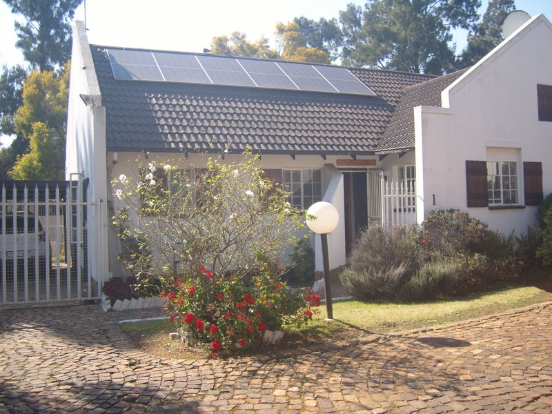 Front elevation of a townhouse featuring a cobblestone driveway, security gate, and roof-mounted solar panels.