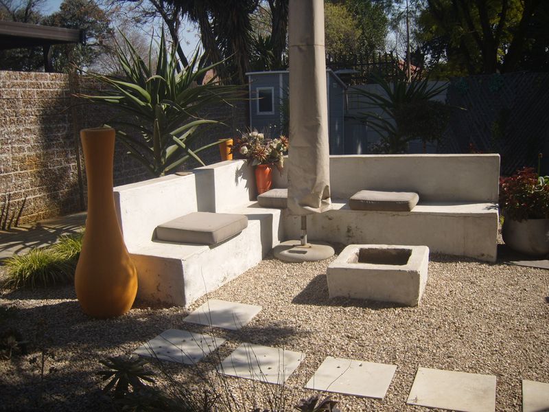 Outdoor patio area featuring built-in concrete seating and a central fire pit, set within a gravel-surfaced garden space.
