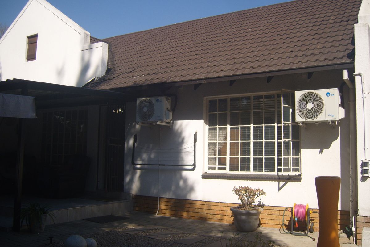 Rear exterior view of the townhouse featuring a tiled roof, paved patio area, and wall-mounted air conditioning units.