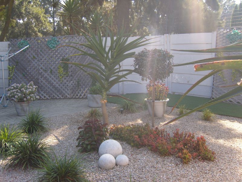 A landscaped garden area featuring a gravel bed, artificial lawn, paved patio section, and a precast concrete boundary wall with lattice privacy screening.