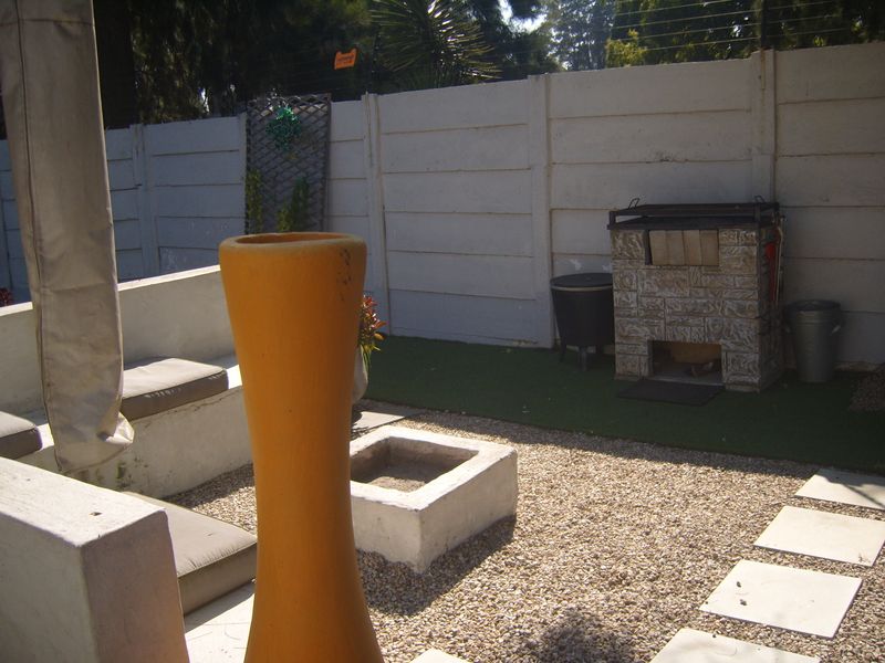 Outdoor patio area featuring a built-in braai, concrete bench seating, a central fire pit, and a mix of artificial grass and gravel landscaping.