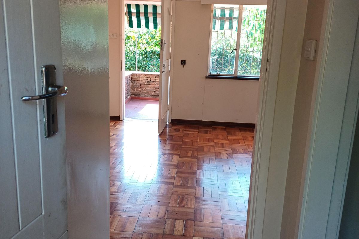 An empty living room featuring classic parquet flooring, security bars on the windows, and direct access to an outdoor patio area.