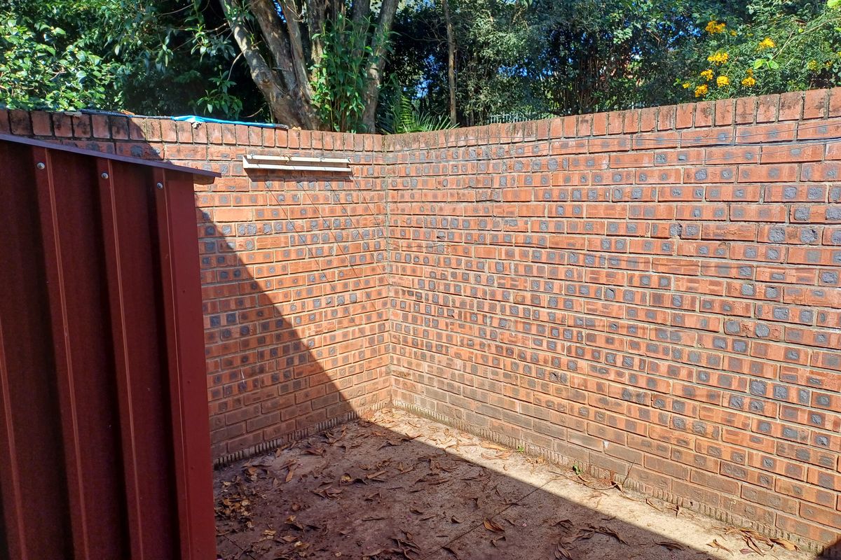 A private rear courtyard area enclosed by high brick boundary walls, featuring a metal storage structure and natural ground surface.