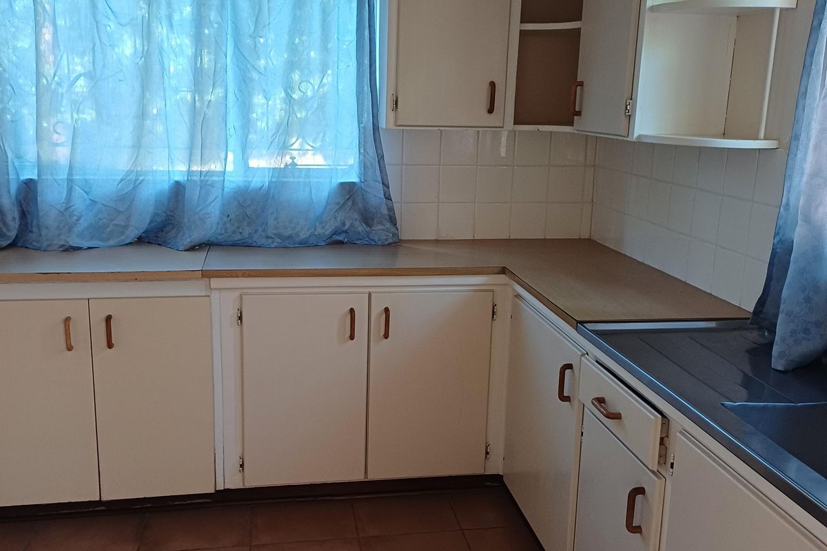 A dated kitchen featuring original cabinetry, laminate countertops, and tiled flooring, offering a blank canvas for a modern renovation.