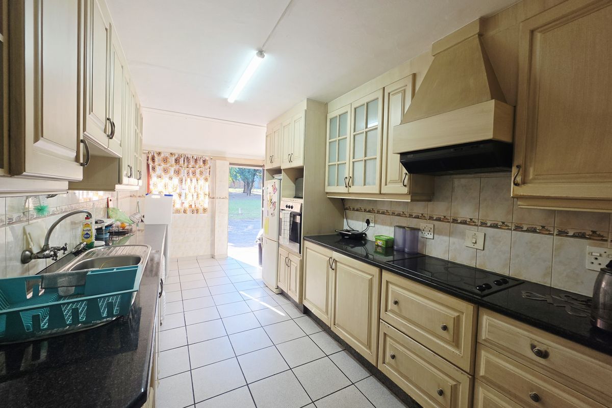 A functional galley-style kitchen featuring built-in cabinetry, granite countertops, integrated oven and hob, and direct access to the exterior.