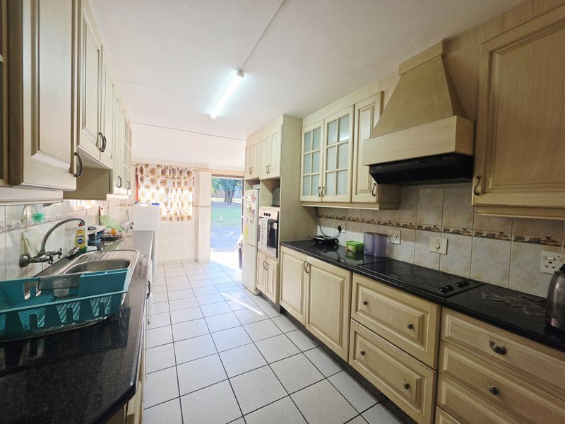 A functional galley-style kitchen featuring built-in cabinetry, granite countertops, integrated oven and hob, and direct access to the exterior.