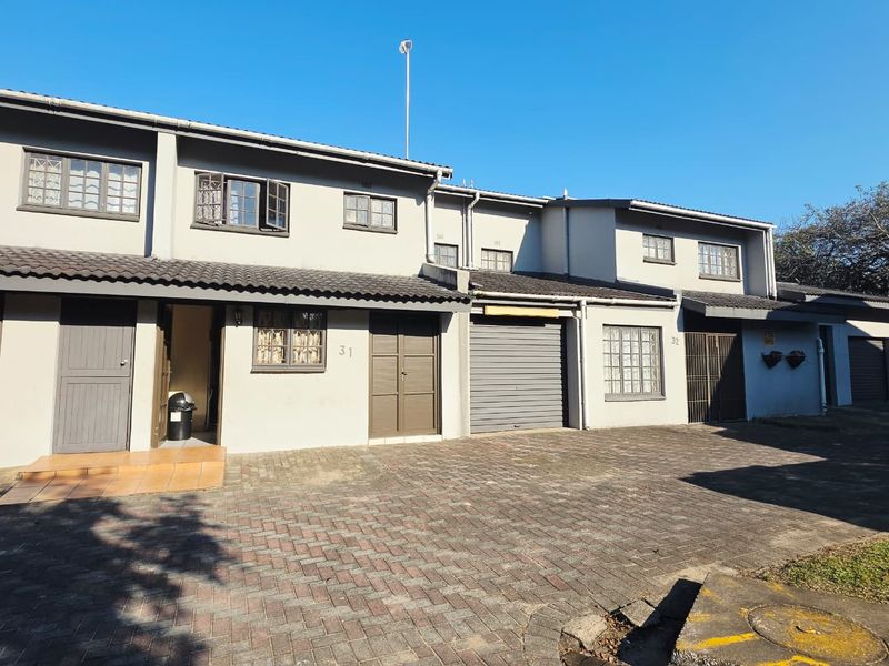Front elevation of a multi-unit residential complex featuring paved driveway access, integrated garage, and tiled entrance porch.